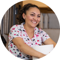 Smiling woman with dark hair and a blouse with a multi-colored hearts pattern