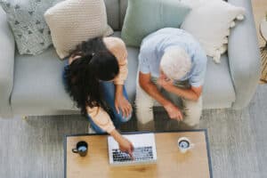 Aerial view of two people sitting on a gray sofa, focused on a laptop on a coffee table.